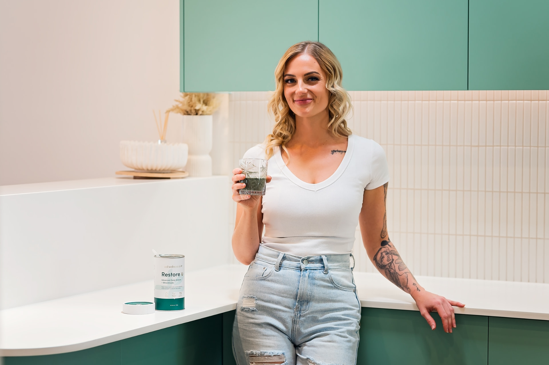 Woman in her kitchen holding a glass of Restore U beside the open Restore U jar